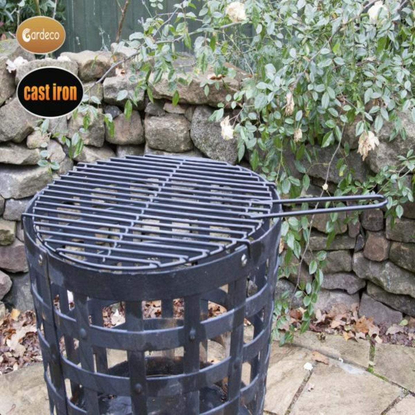 Cast iron grill on a stone patio with a stone wall and plants in the background