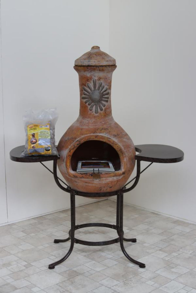 Terracotta chiminea with black metal stand on a tiled floor against a white wall