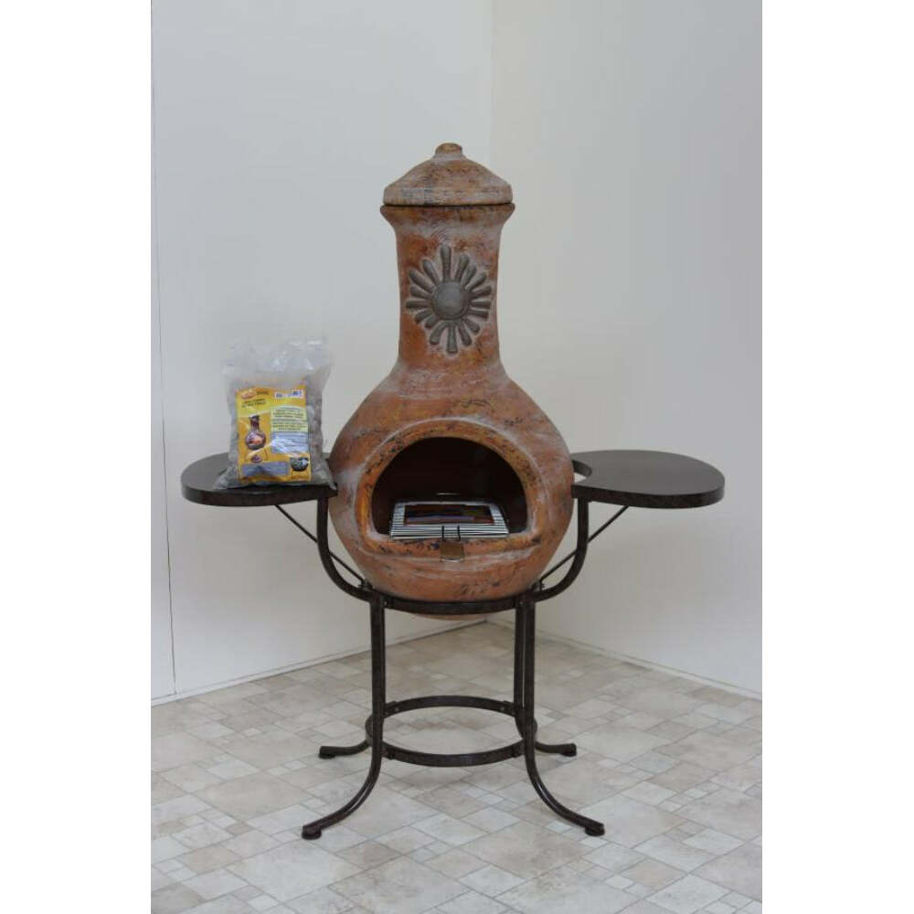 Terracotta chiminea with black metal stand on a tiled floor against a white wall