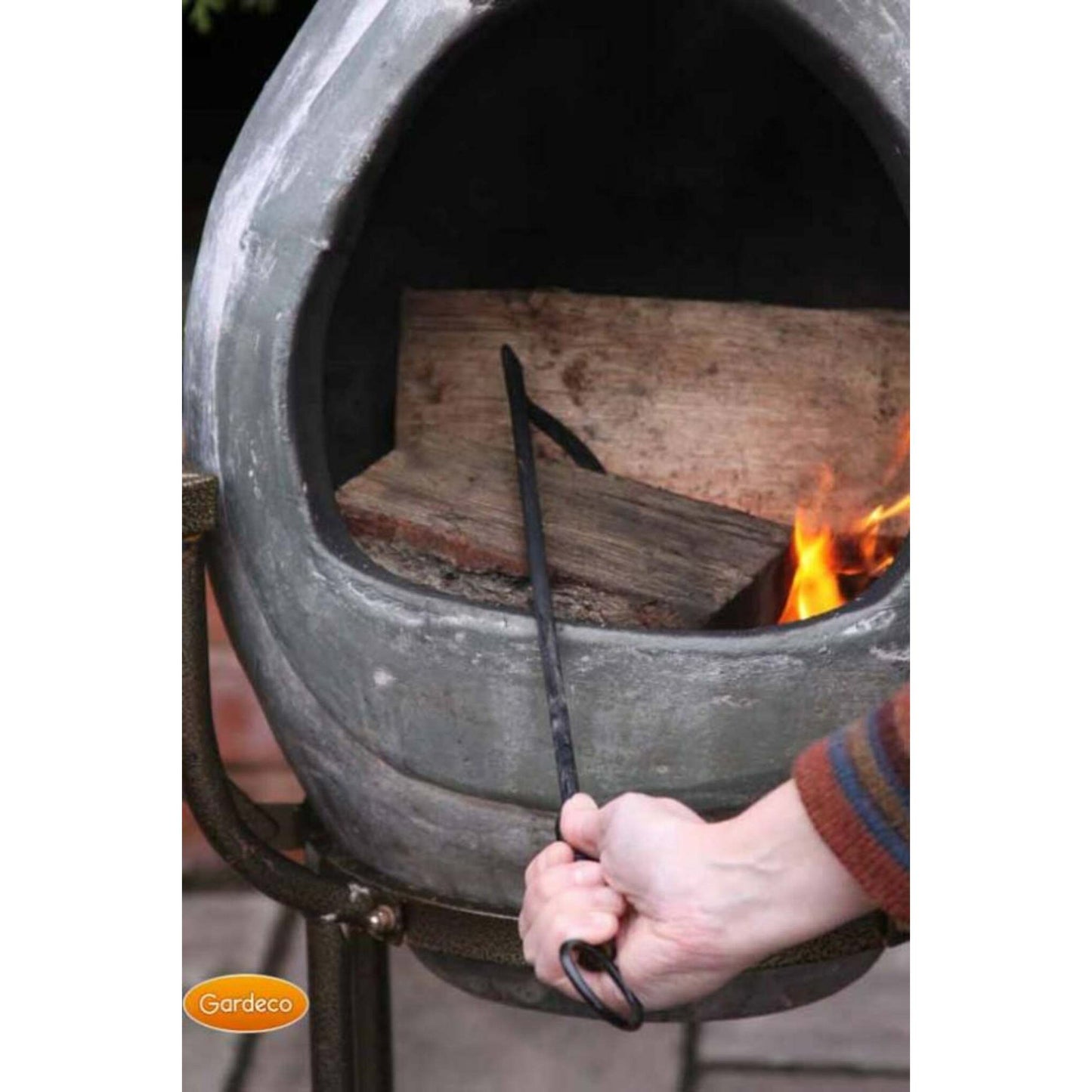 Person using a fire poker to tend to wood in a Gardeco fire pit.