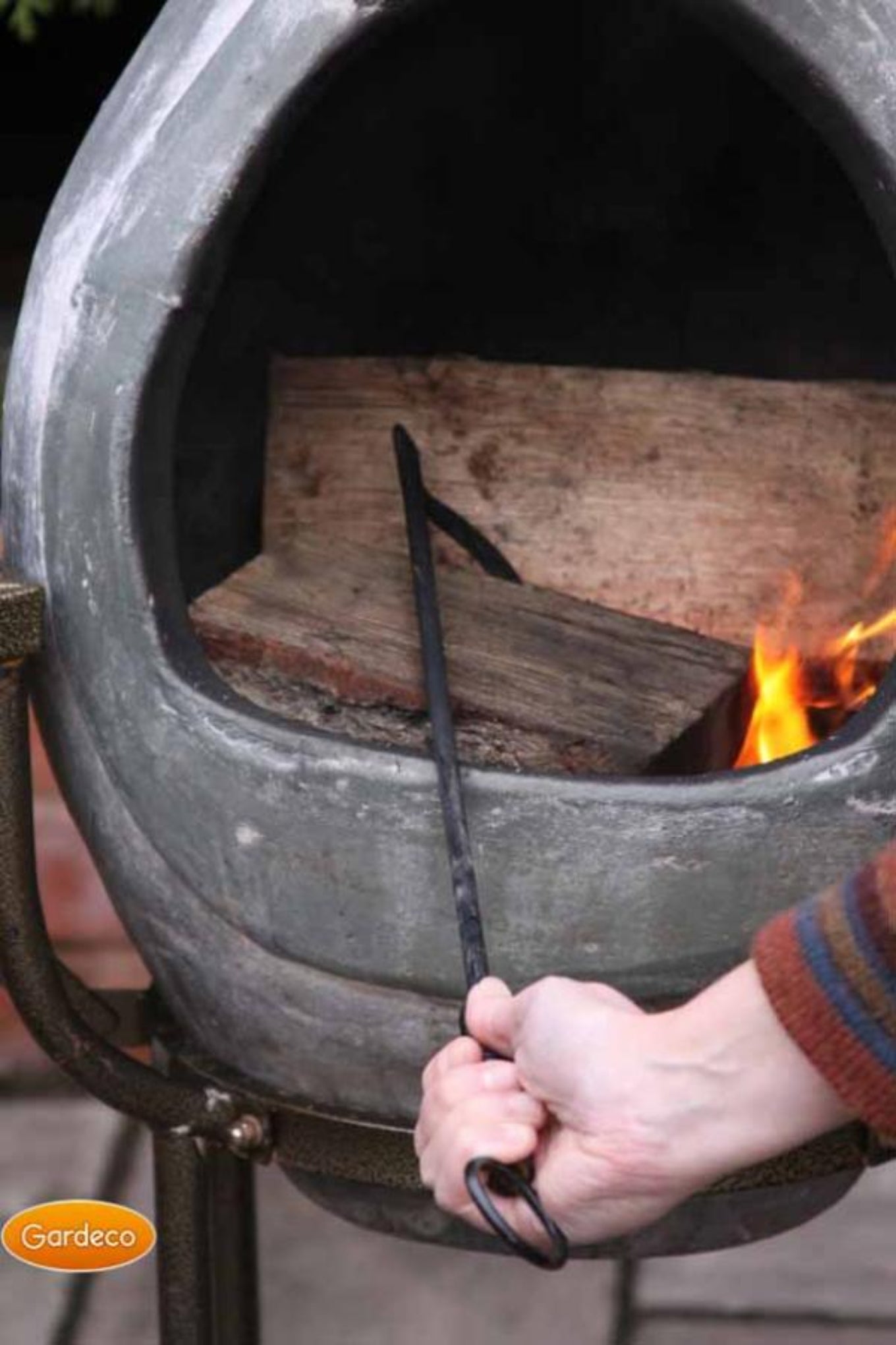 Person using a fire poker to tend to wood in a Gardeco fire pit.