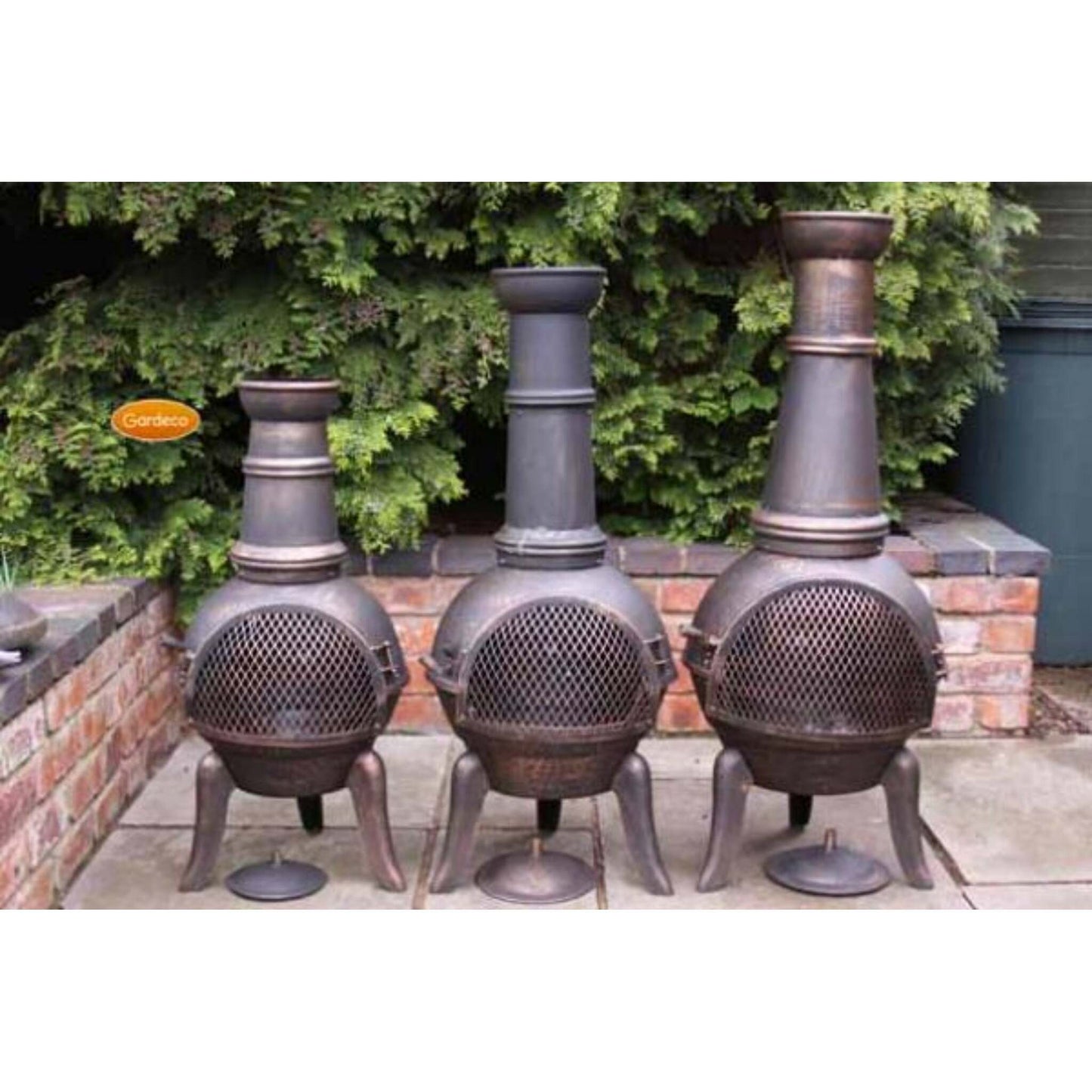 Three metal chimineas on a patio with greenery in the background