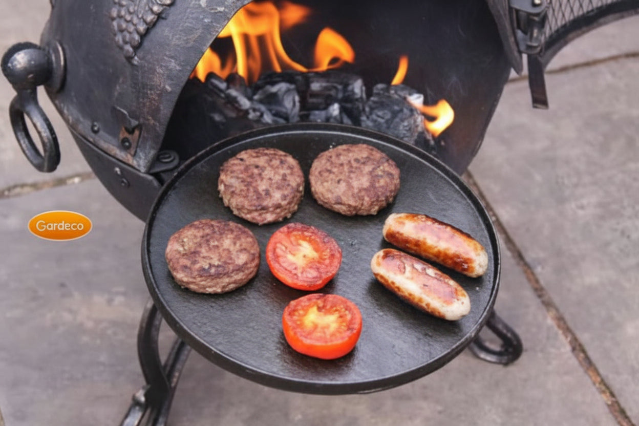 Hamburgers and sausages cooking on a cast iron griddle over an open fire.
