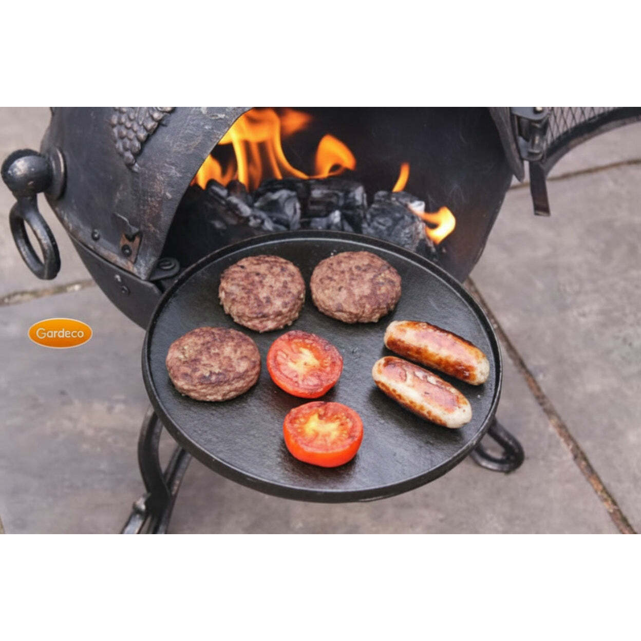 Hamburgers and sausages cooking on a cast iron griddle over an open fire.