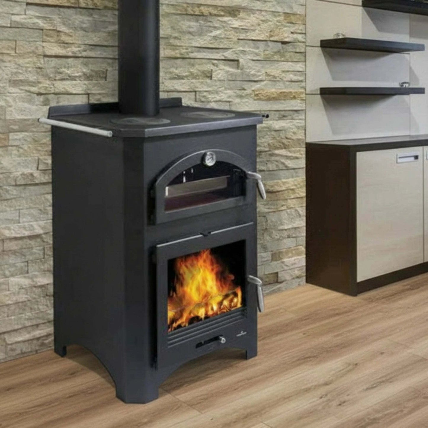 Black Bronpi Monza wood stove with fire burning inside, against a stone wall.