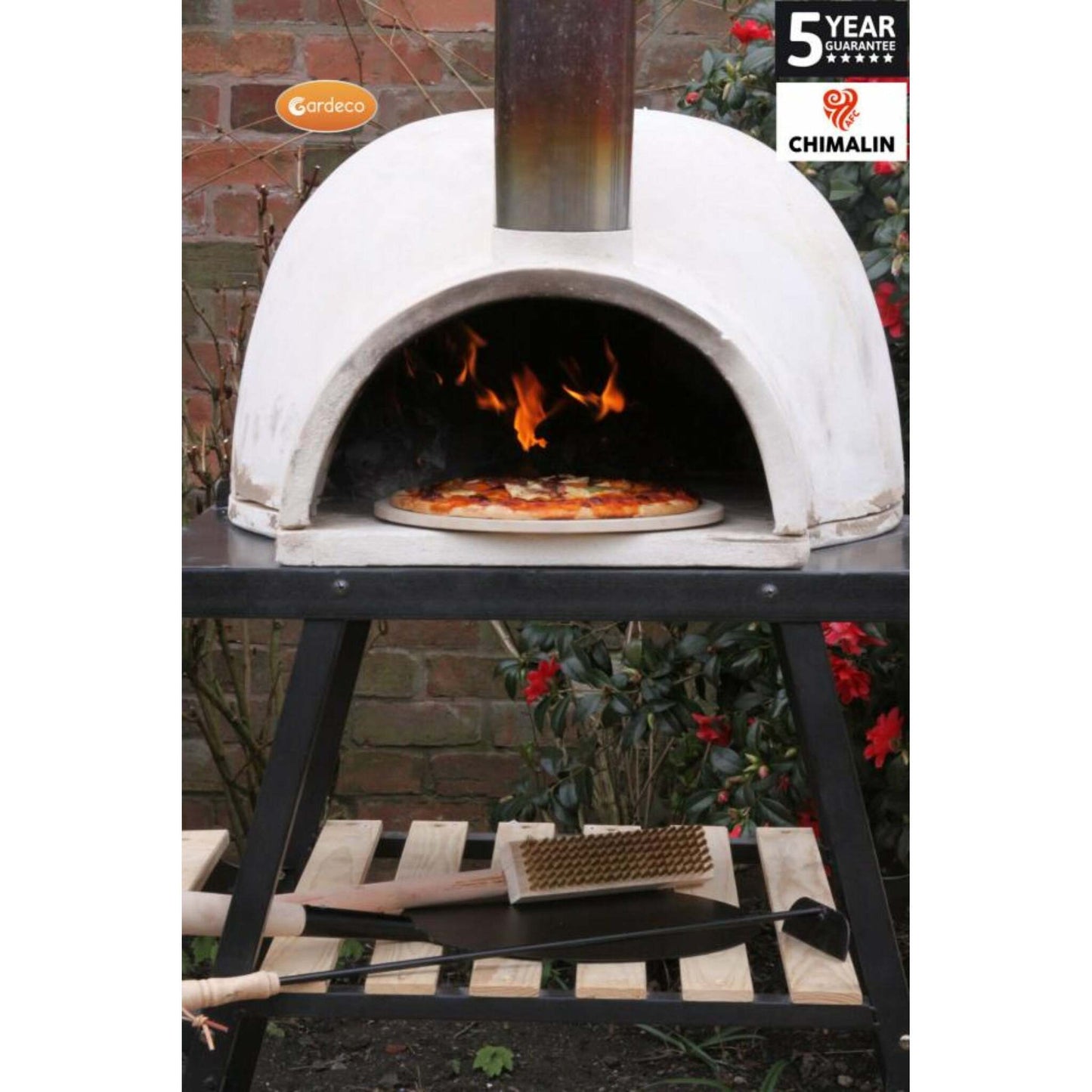 Outdoor pizza oven with a pizza being cooked, surrounded by garden elements.