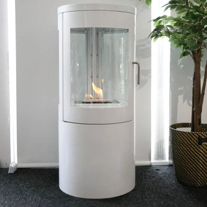 White cylindrical fireplace with glass door on a dark floor, plant in the background