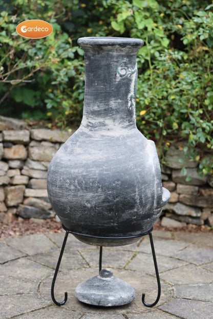 Back of Iguana X-Large Mexican Chiminea Grey | Handmade Clay on a stand with a stone wall and greenery in the background