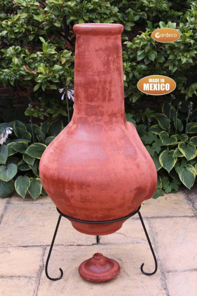 Terracotta chiminea with metal stand on a patio with greenery in the background