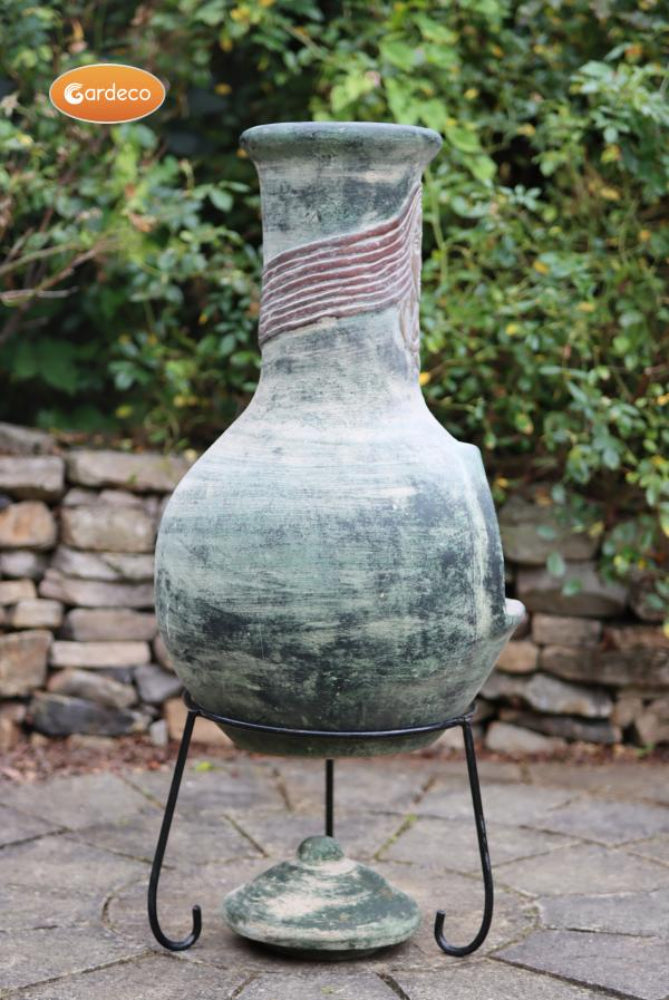 Decorative ceramic vase on a stand with a stone wall and greenery background