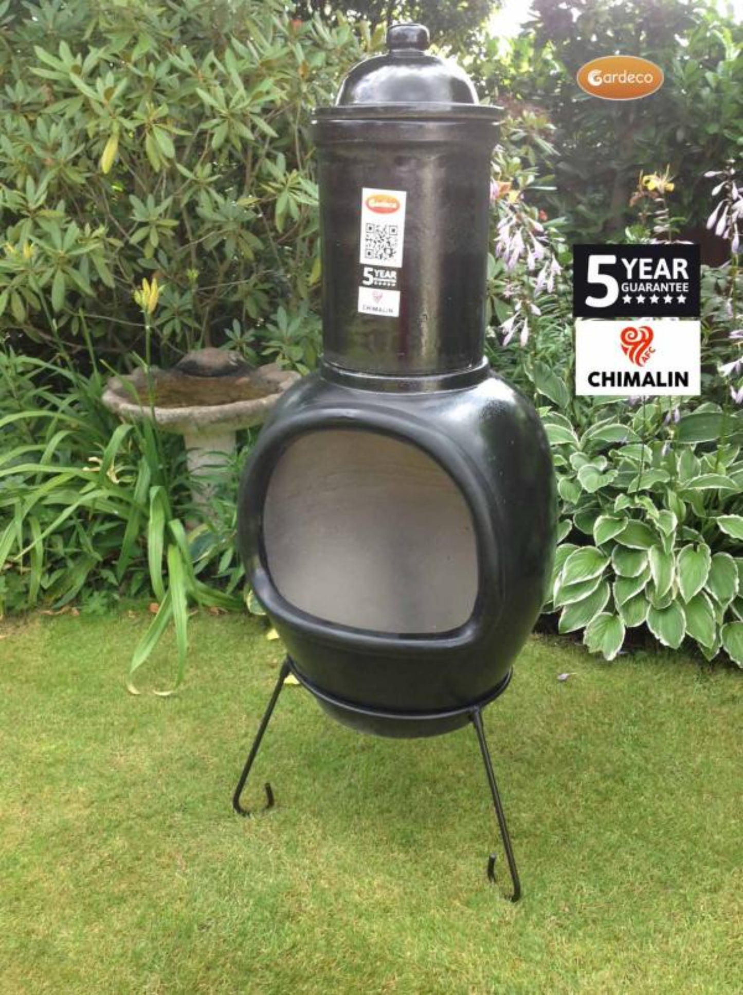 Black chiminea on a grassy area with garden plants in the background
