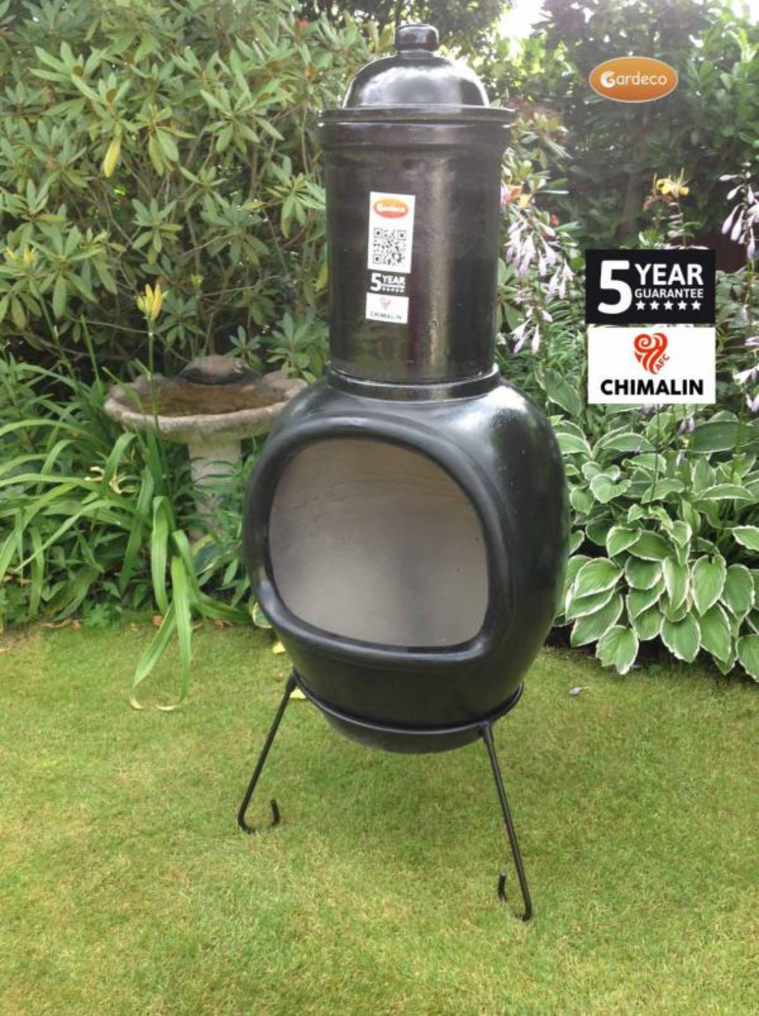 Black chiminea on a grassy area with garden plants in the background