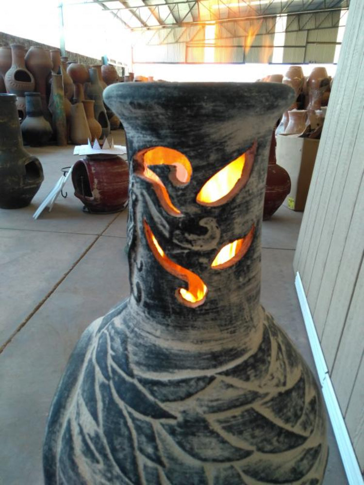 Ceramic chiminea with dragon design glowing inside, surrounded by other chimineas.