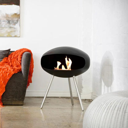Cocoon Terra Freestanding Bioethanol Fireplace - Matte Black Steel Legs in a white room with grey sofa and orange throw.