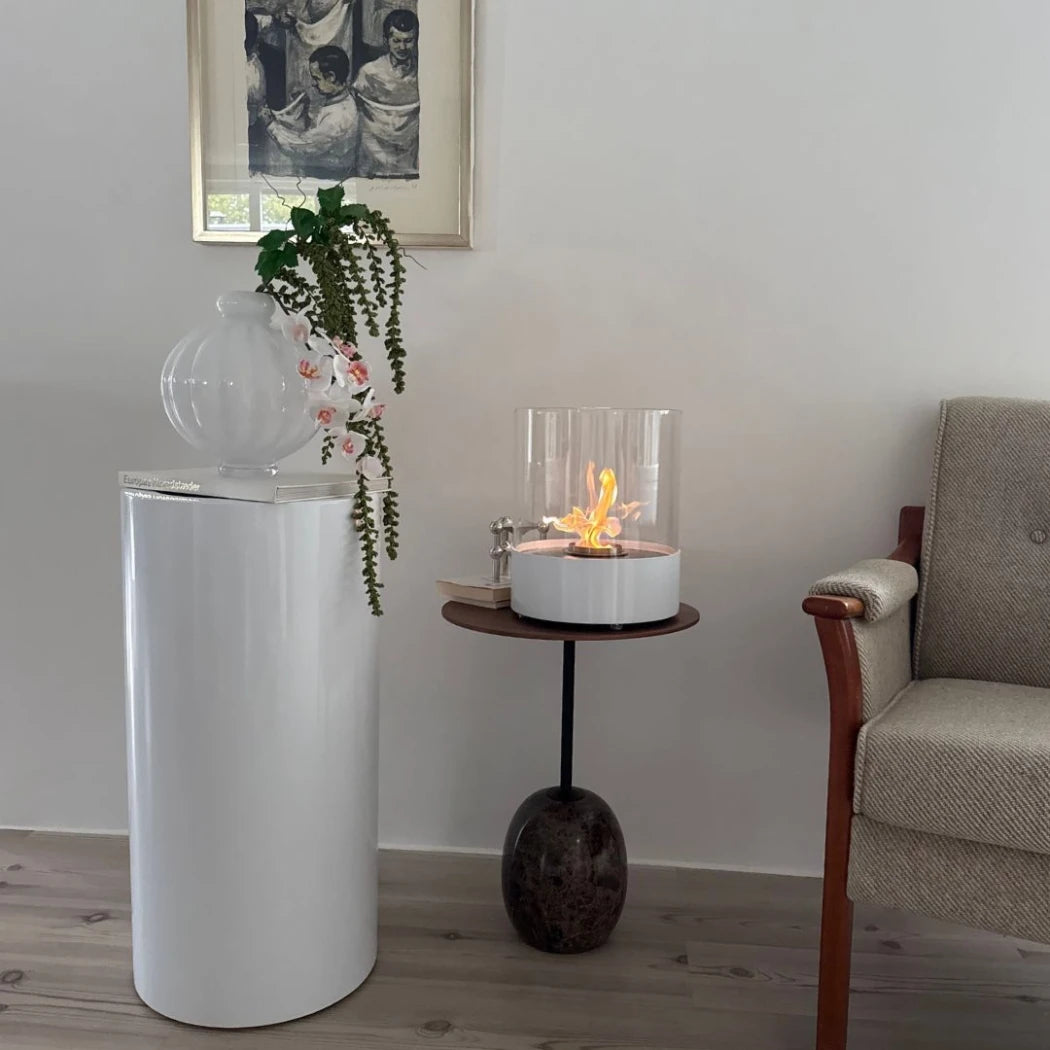 Modern living room with a white cylindrical object, plant, and small table with a fire pit.