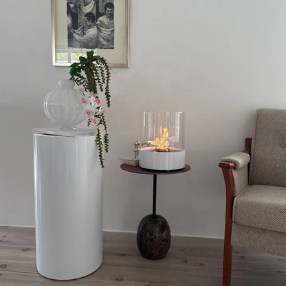 Modern living room with a white cylindrical object, plant, and small table with a fire pit.
