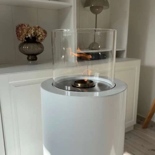 White portable fireplace with clear glass cover on a wooden floor.