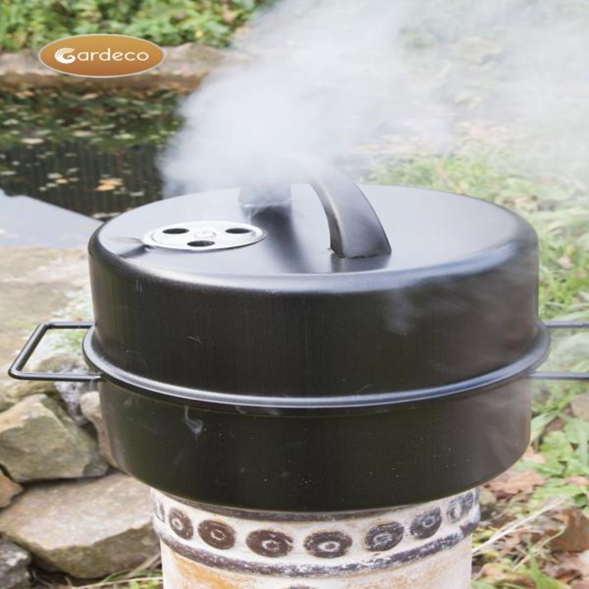 Black smoker with smoke rising, set against a natural outdoor background.