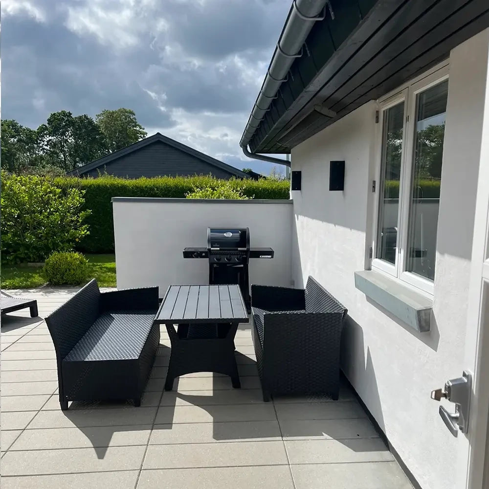 Outdoor patio area with black furniture and grill next to a white house.