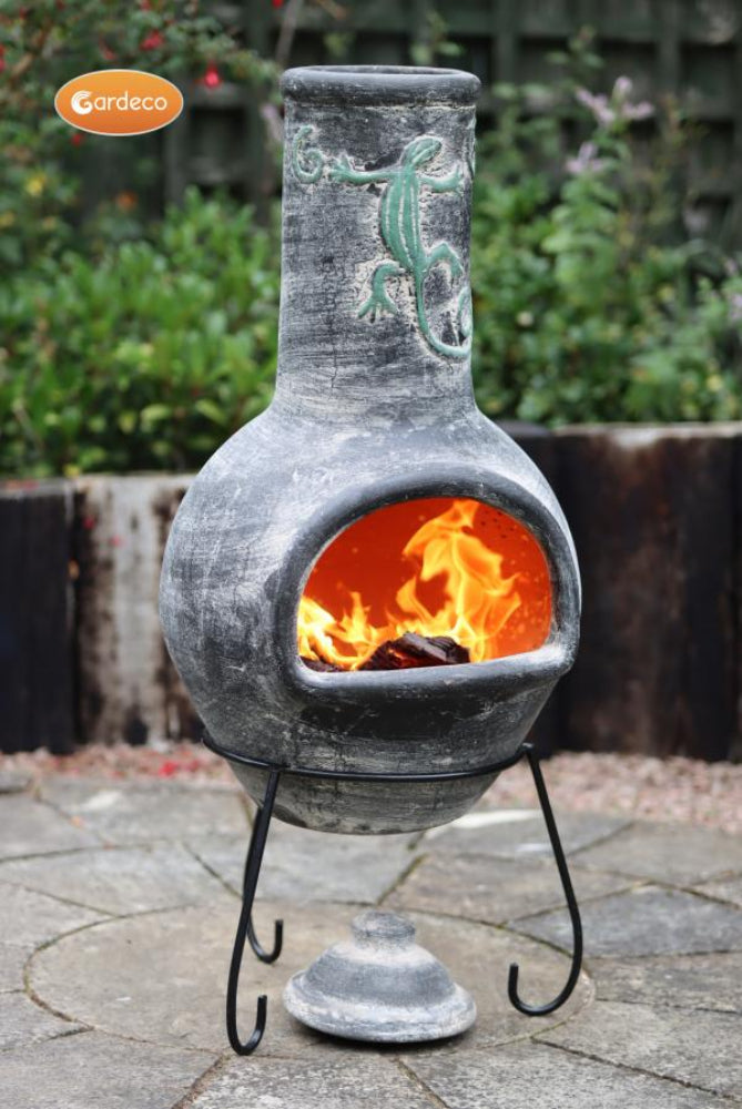 Decorative outdoor chiminea with flames inside, featuring a lizard design on a blurred garden background.