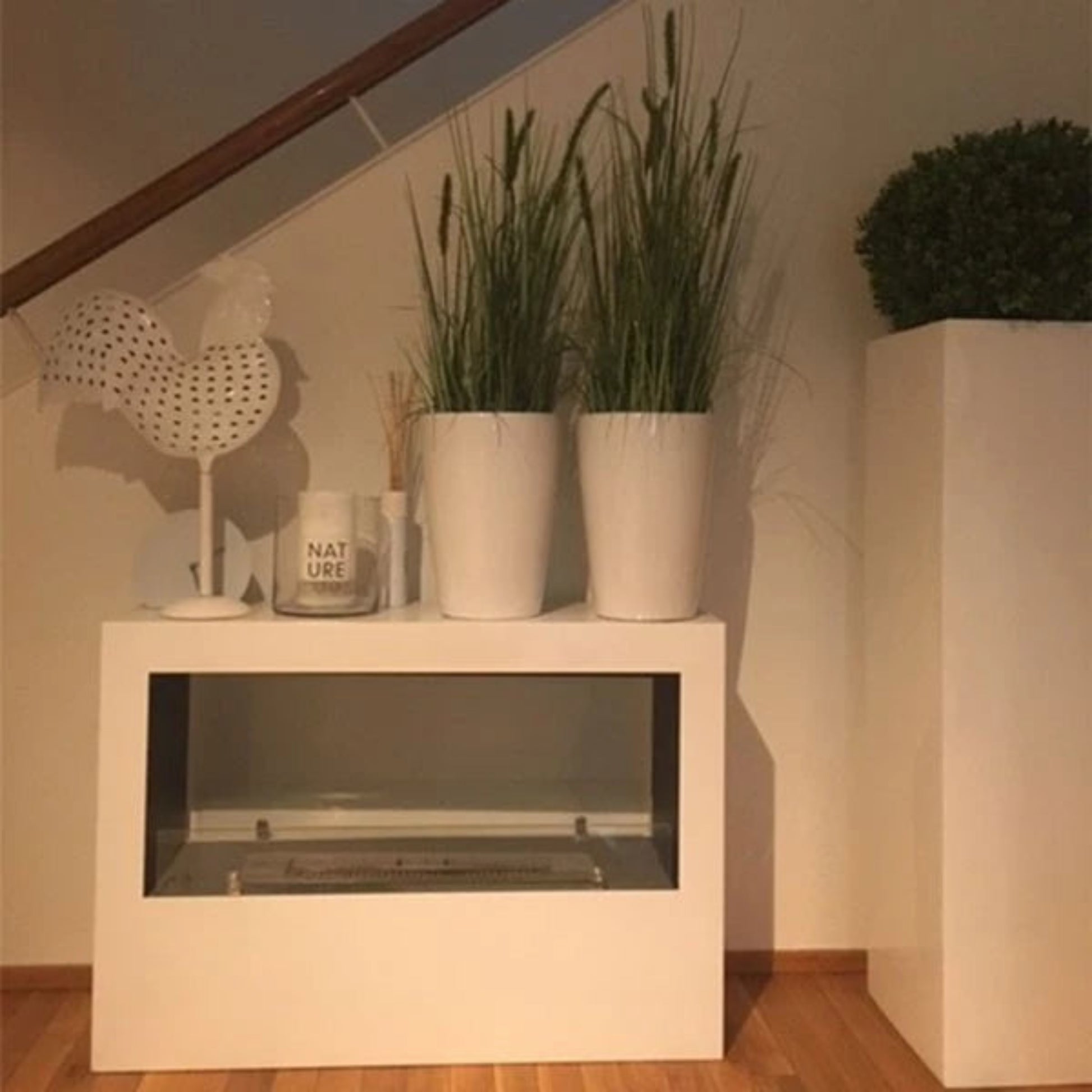 White Lansing two sided bioethanol fire with decorative items including potted plants and a mug on a wooden floor.