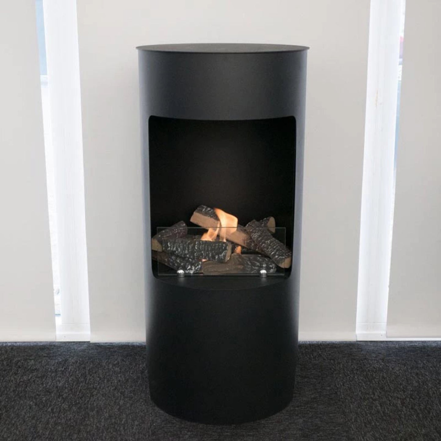 Modern black freestanding fireplace with visible flames and logs inside, set against a neutral background.