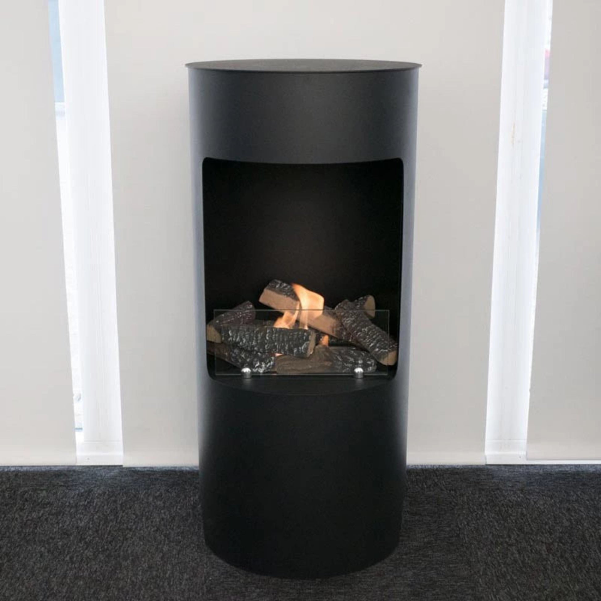 Modern black freestanding fireplace with visible flames and logs inside, set against a neutral background.