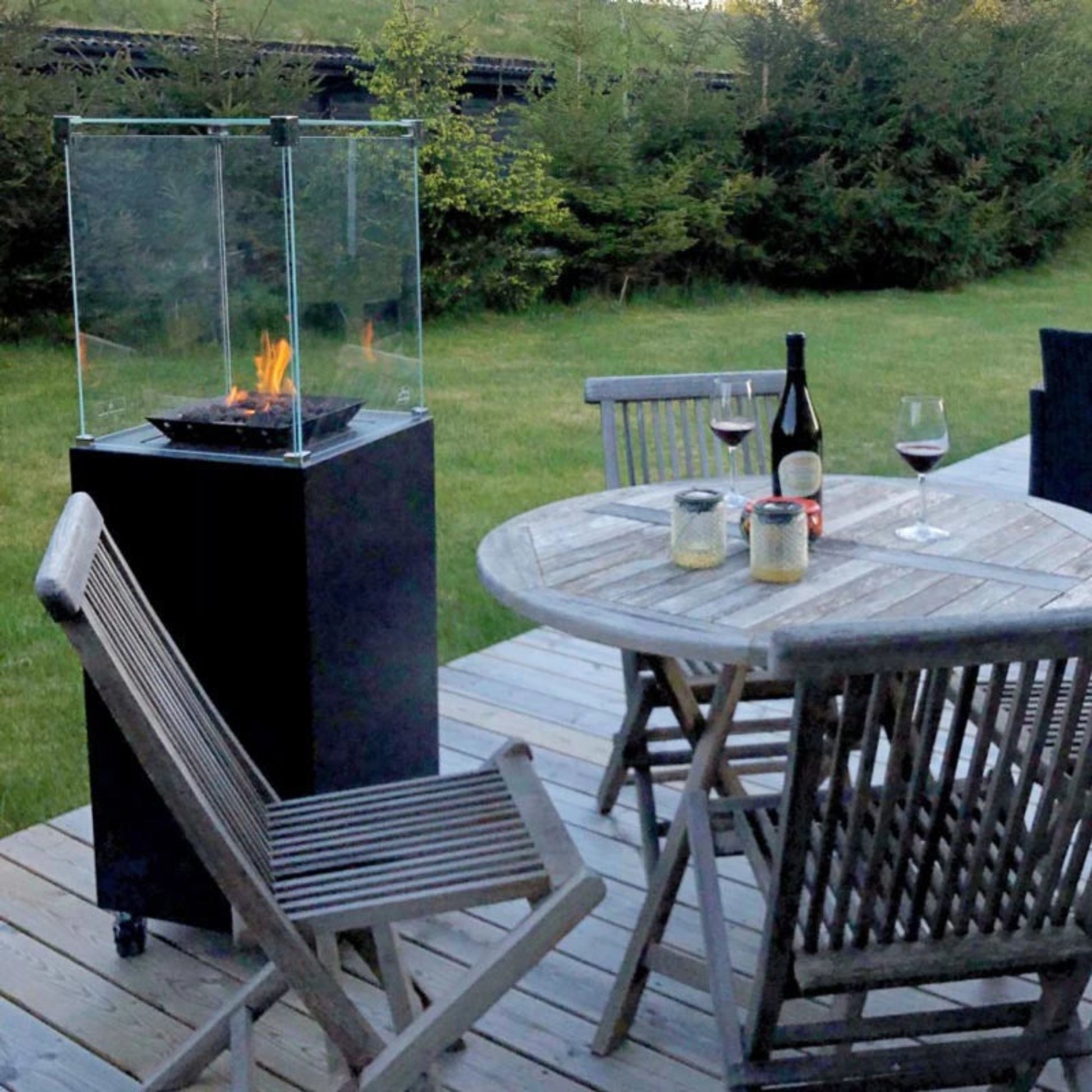 Outdoor patio setting with a fire pit, table, chairs, and wine glasses on a wooden deck.