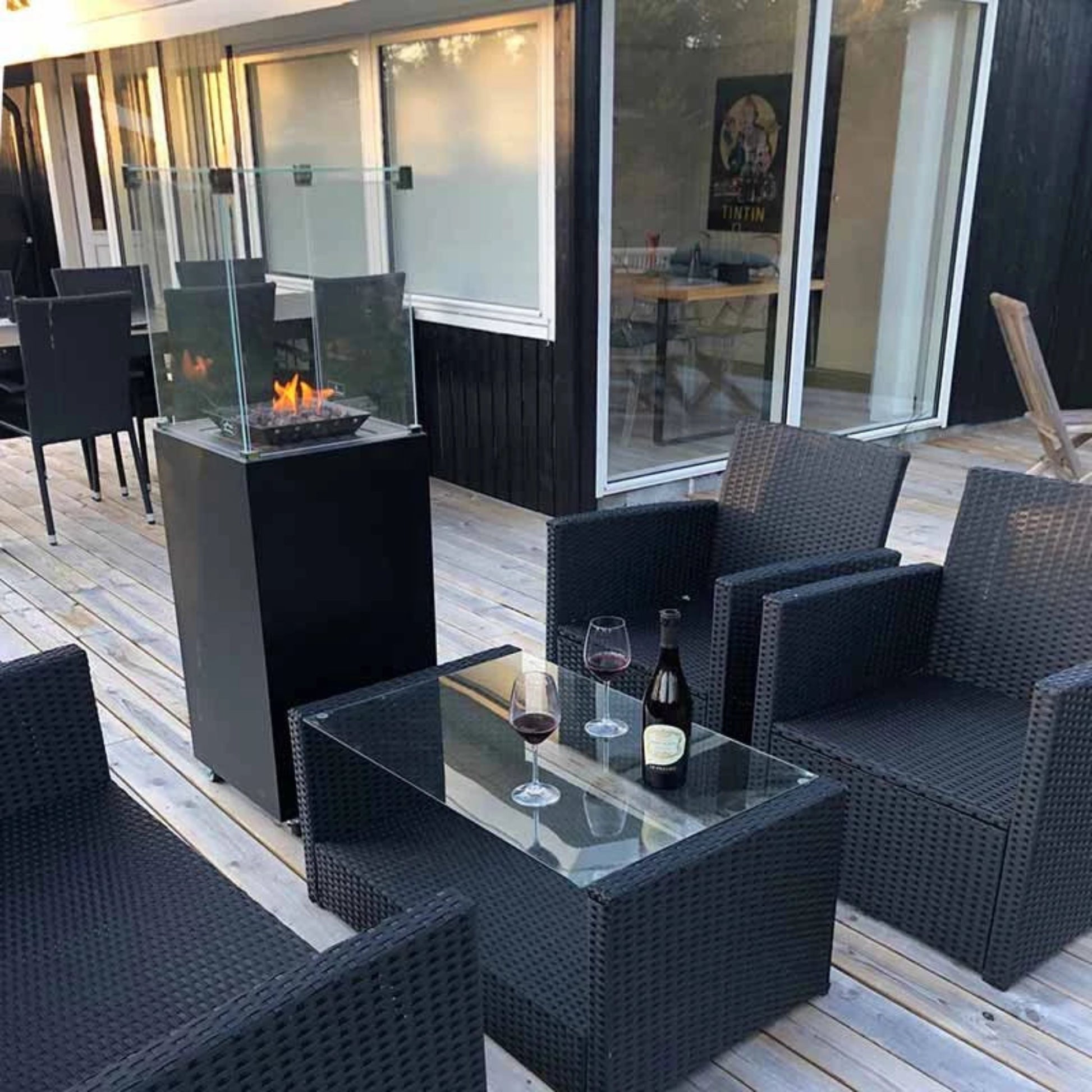 Outdoor patio setup with black chairs, glass table, and fire pit on a wooden deck.