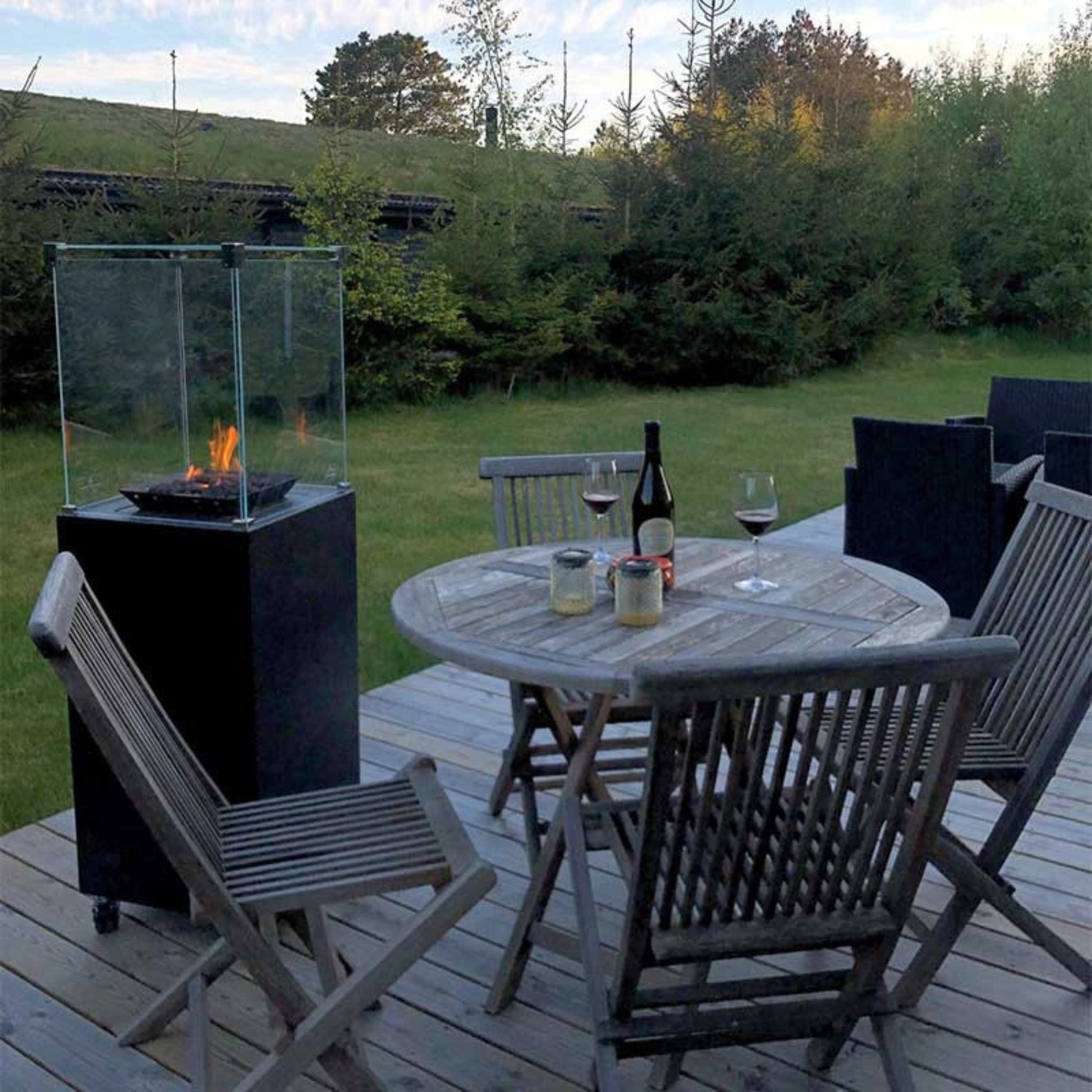 Outdoor patio setting with a fire pit, table, chairs, and wine glasses on a wooden deck.