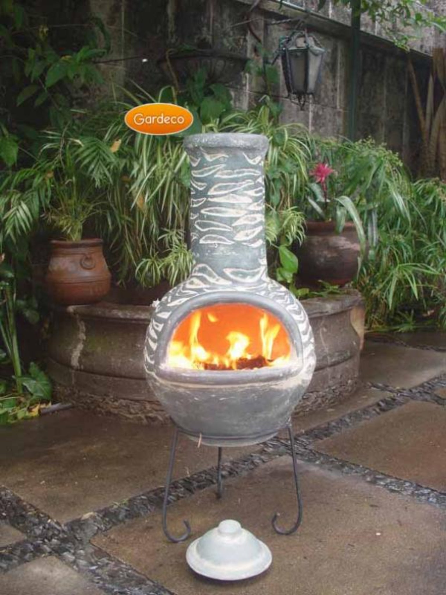 Decorative outdoor fireplace with flames, surrounded by plants and a stone wall.