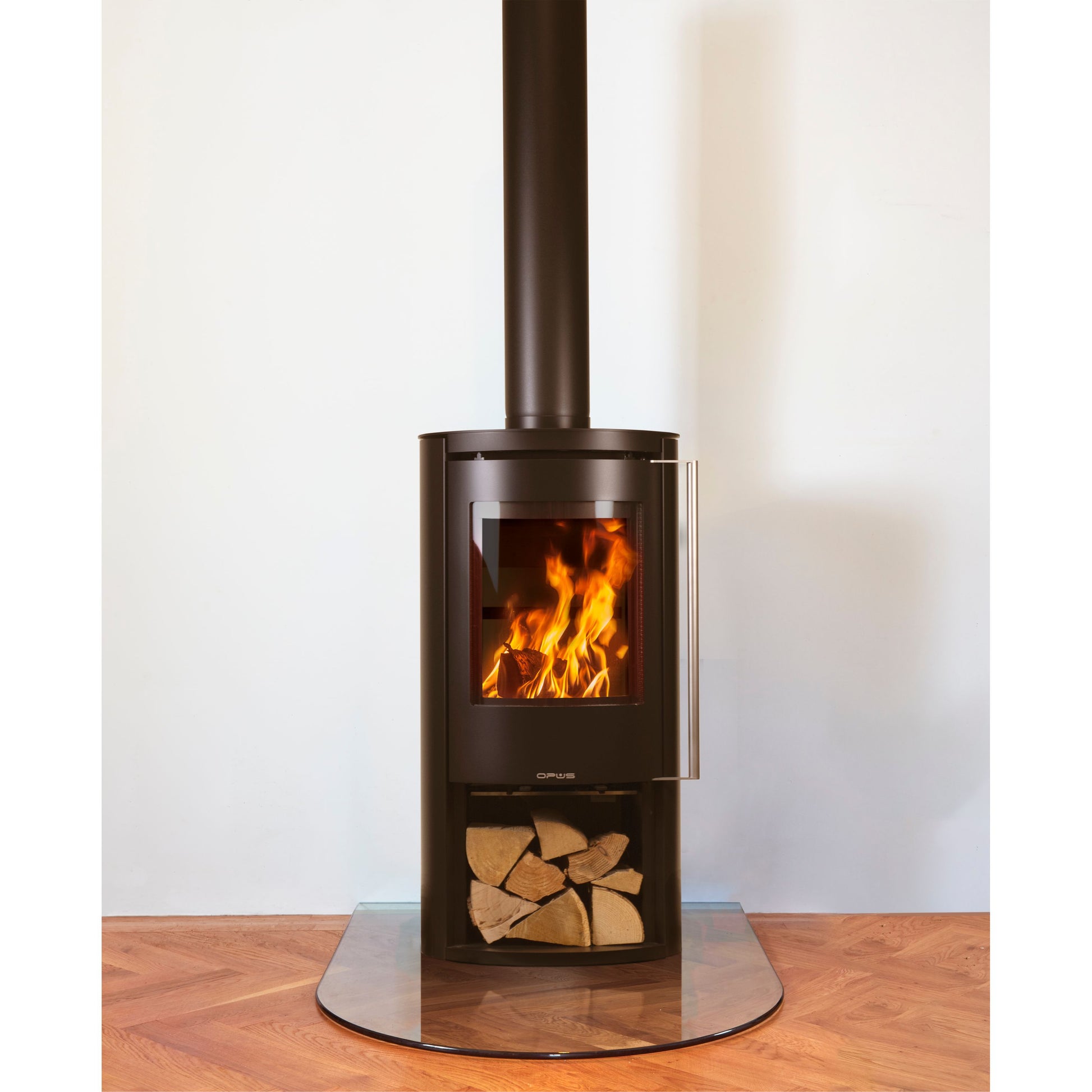 Opus Aria wood stove with flames and log store on a wooden floor against a white wall
