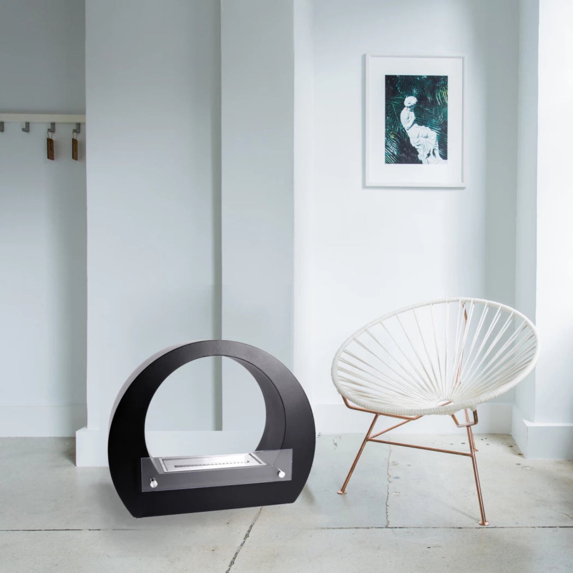 ScandiFlames Dallas Round Bioethanol Fireplace – Black in a white room with a piece of modern art and a photo of a lady.