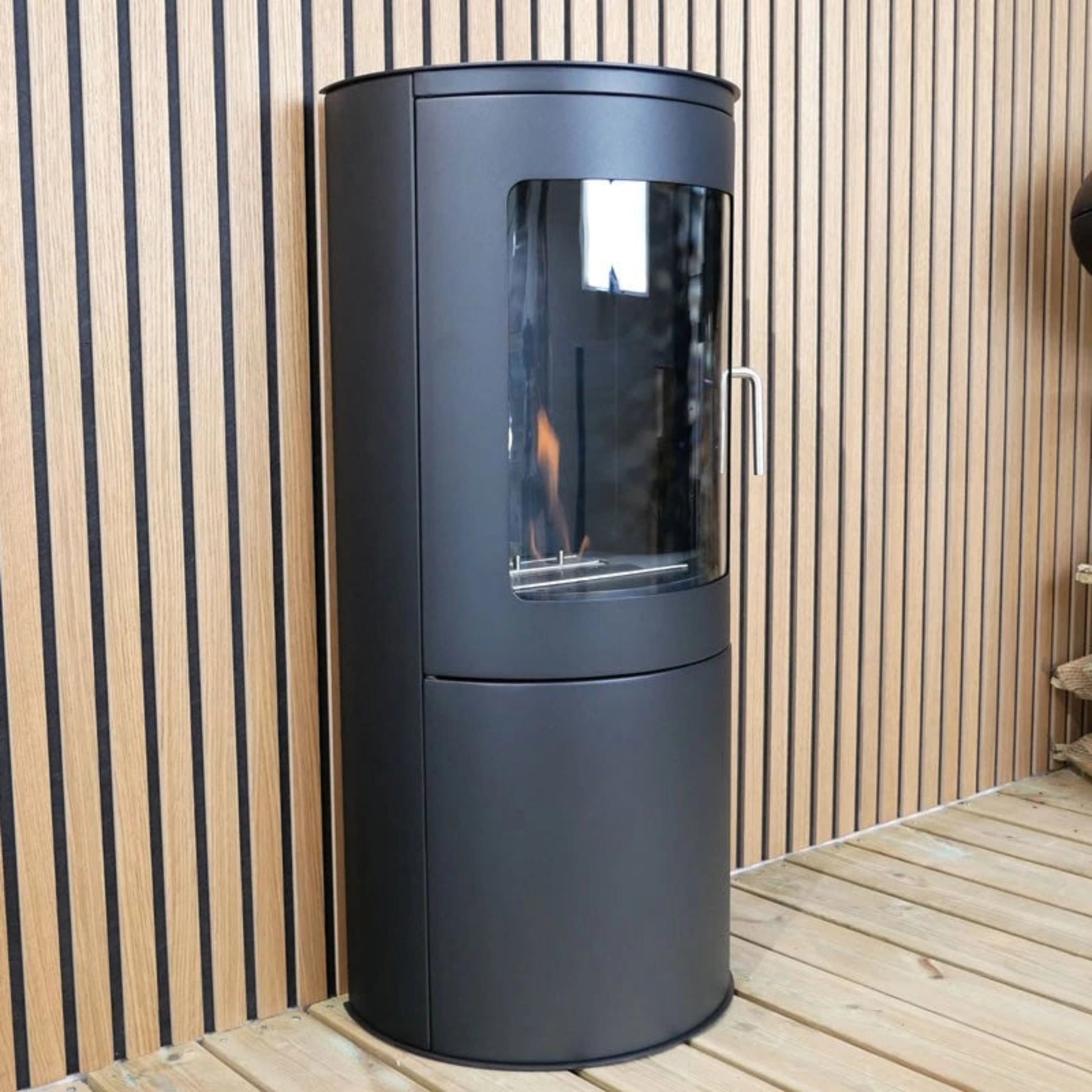 Modern black bioethenol fireplace with glass door on a wooden deck.