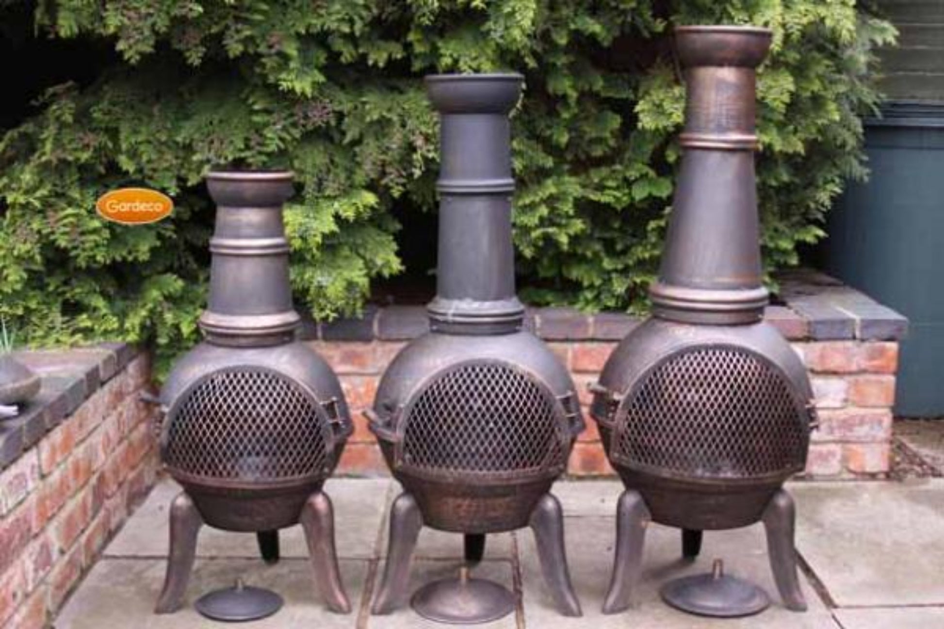 Three metal chimineas on a patio with greenery in the background