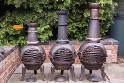 Three metal chimineas on a patio with greenery in the background