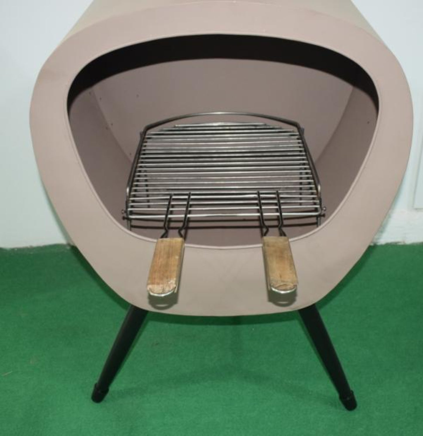 Stalla Chiminea stove with a metal grate and wooden handles on a green surface.