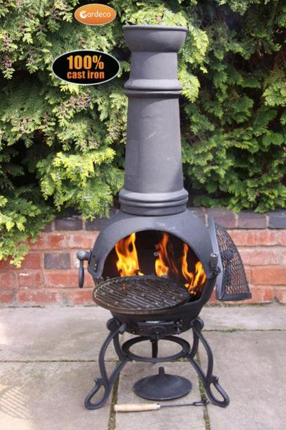 Cast iron chiminea with flames against a green hedge and brick wall background