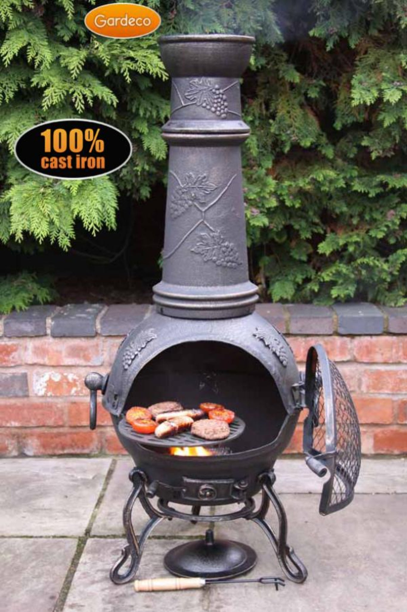 Cast iron chiminea with food on a patio, surrounded by greenery.