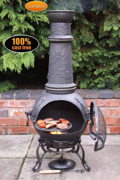 Cast iron chiminea with food on a patio, surrounded by greenery.