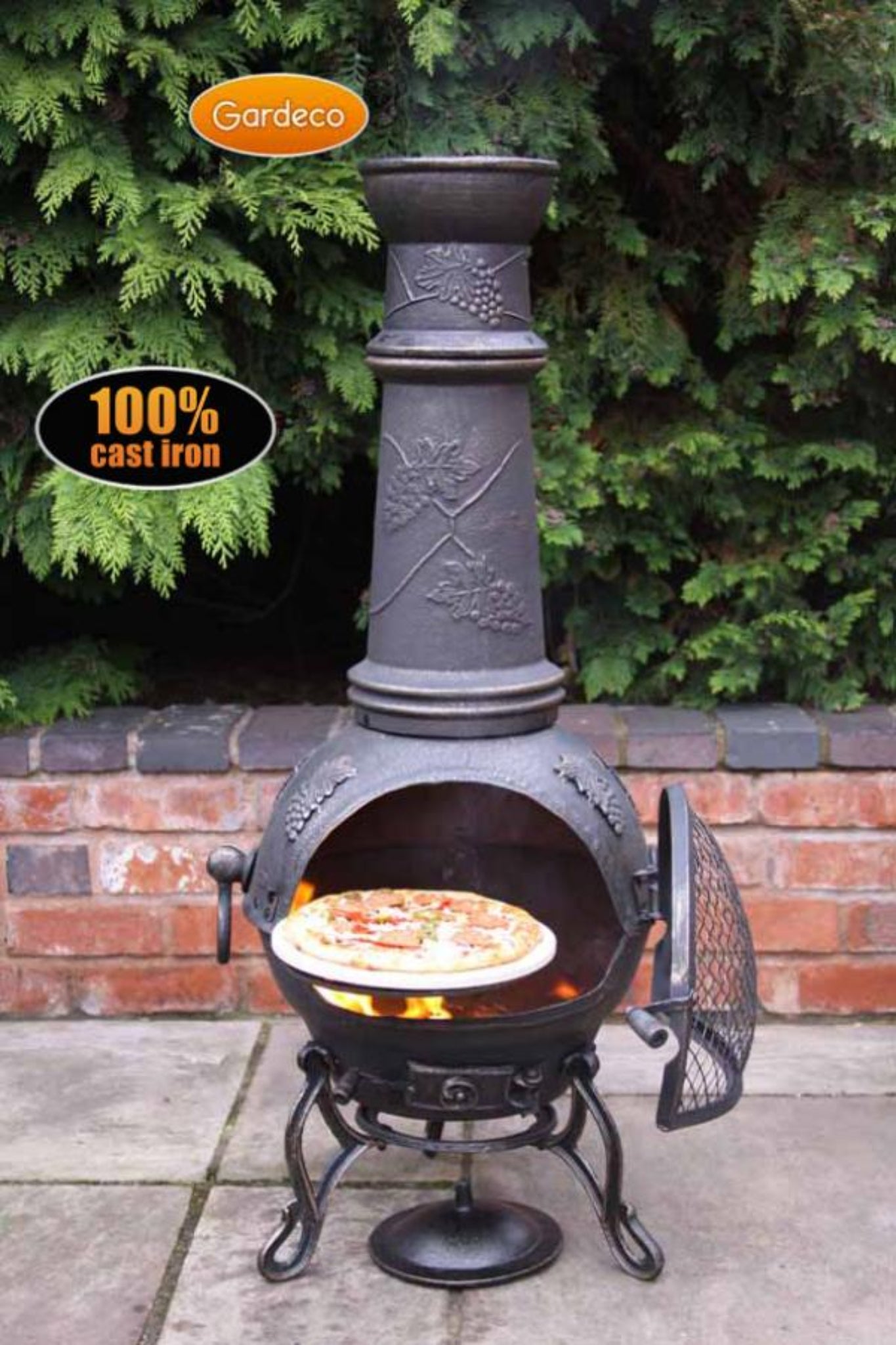 Cast iron chiminea with pizza inside, branded 'Gardeco', on a patio with greenery in the background.
