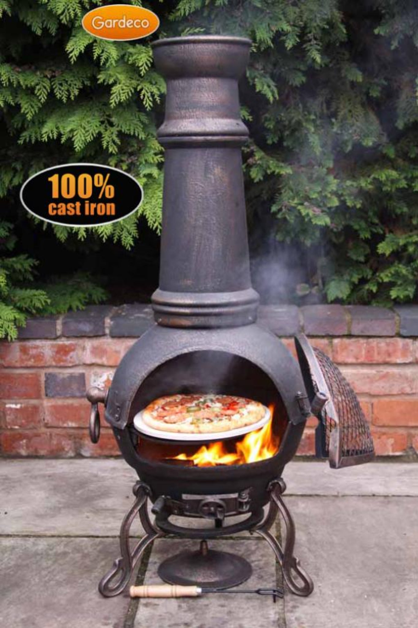 Cast iron chiminea with pizza inside, surrounded by greenery and a brick wall.