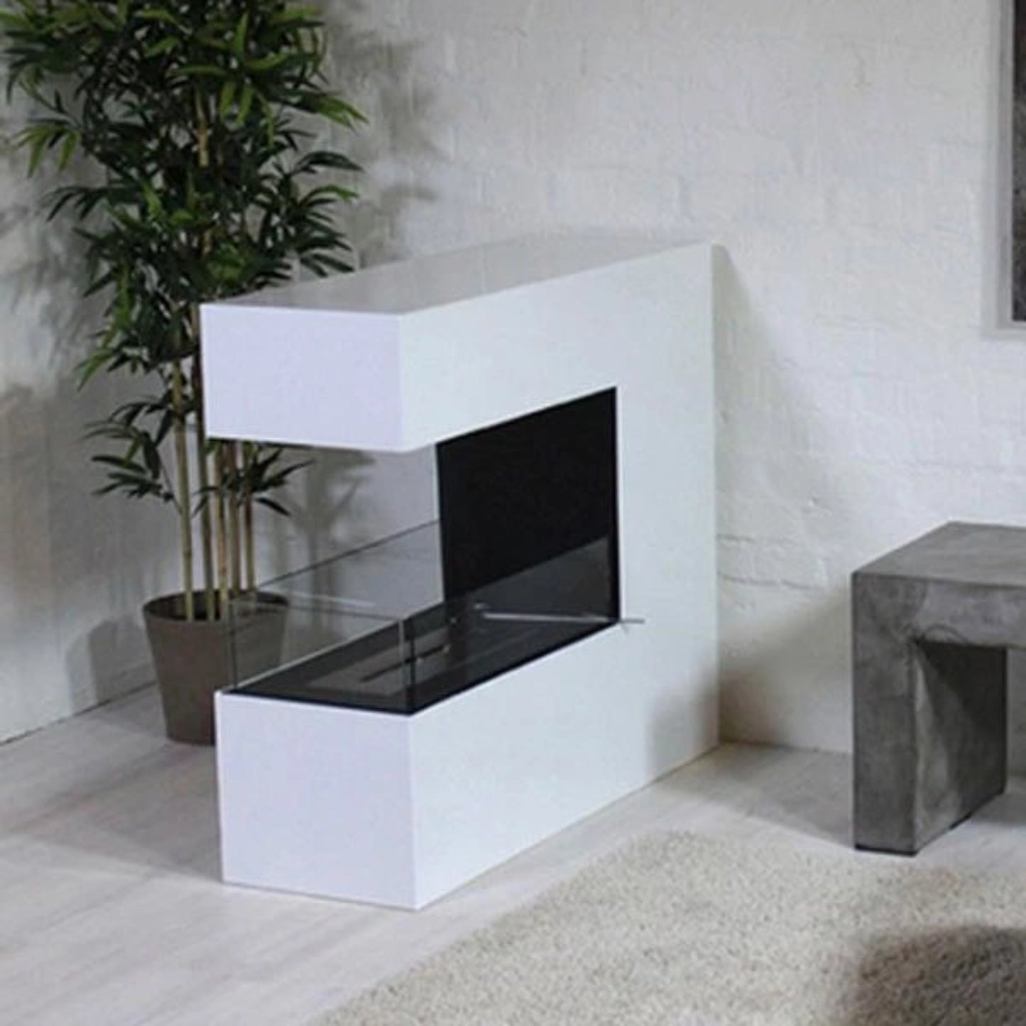 Modern white 3-sided bioethanol stove in a room with a plant and concrete bench.