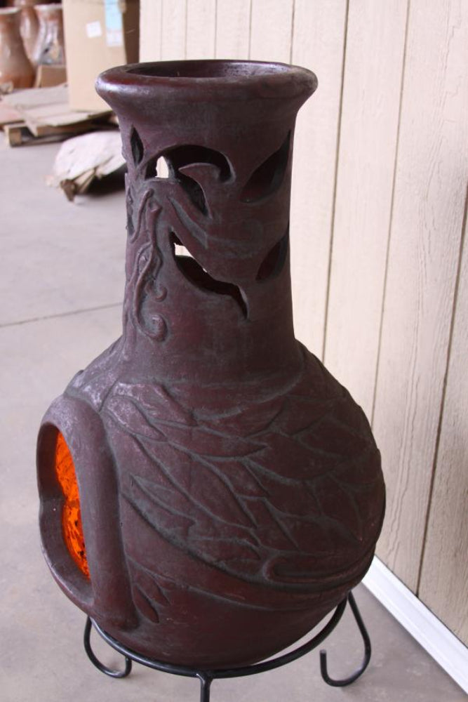 Decorative ceramic chiminea with cut-out designs on a stand against a wooden wall.