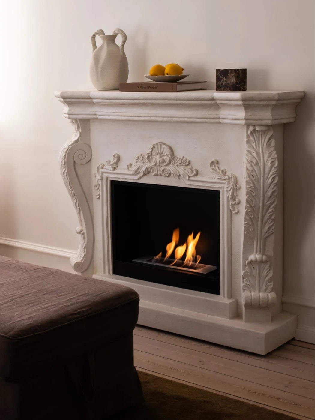 Decorative fireplace with a mantel displaying a vase, fruit, and books in a room.