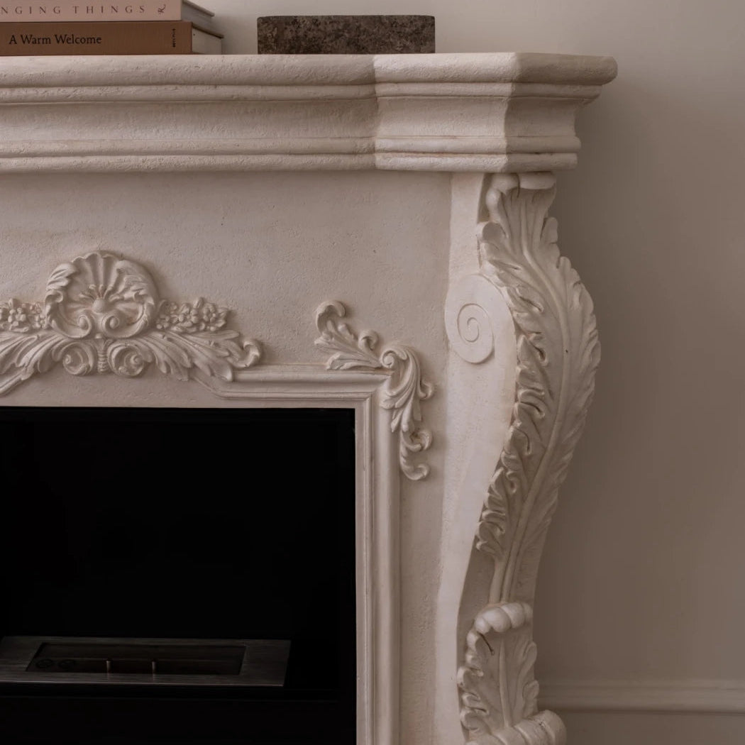 Decorative white fireplace with intricate carvings on a plain wall.