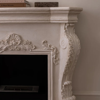 Decorative white fireplace with intricate carvings on a plain wall.