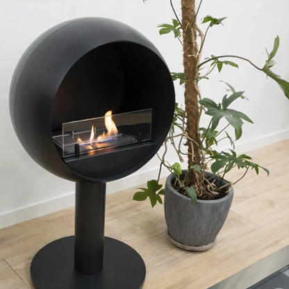 Modern black spherical fireplace on a wooden floor with a plant nearby