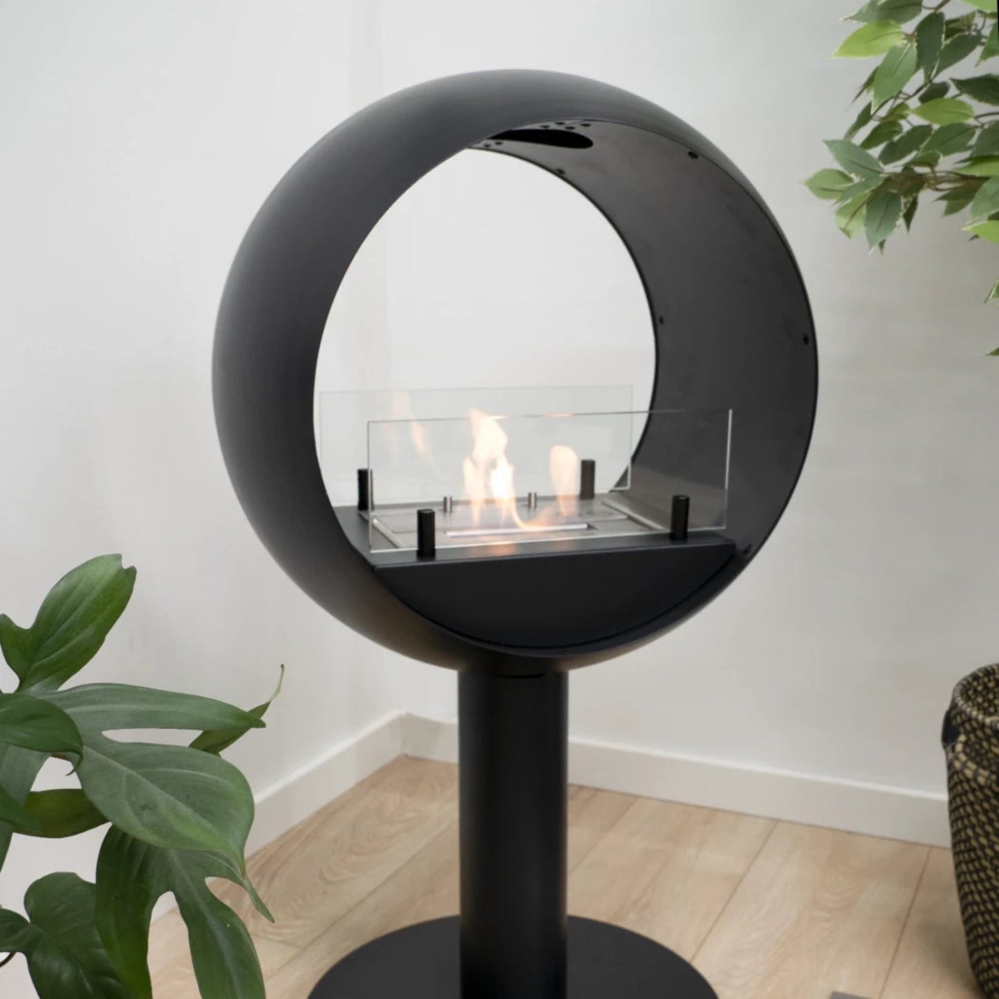 Modern black circular fireplace with flames on a light wood floor.