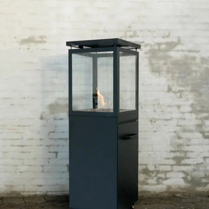 Black outdoor fire pit with glass cover against a textured white brick wall.
